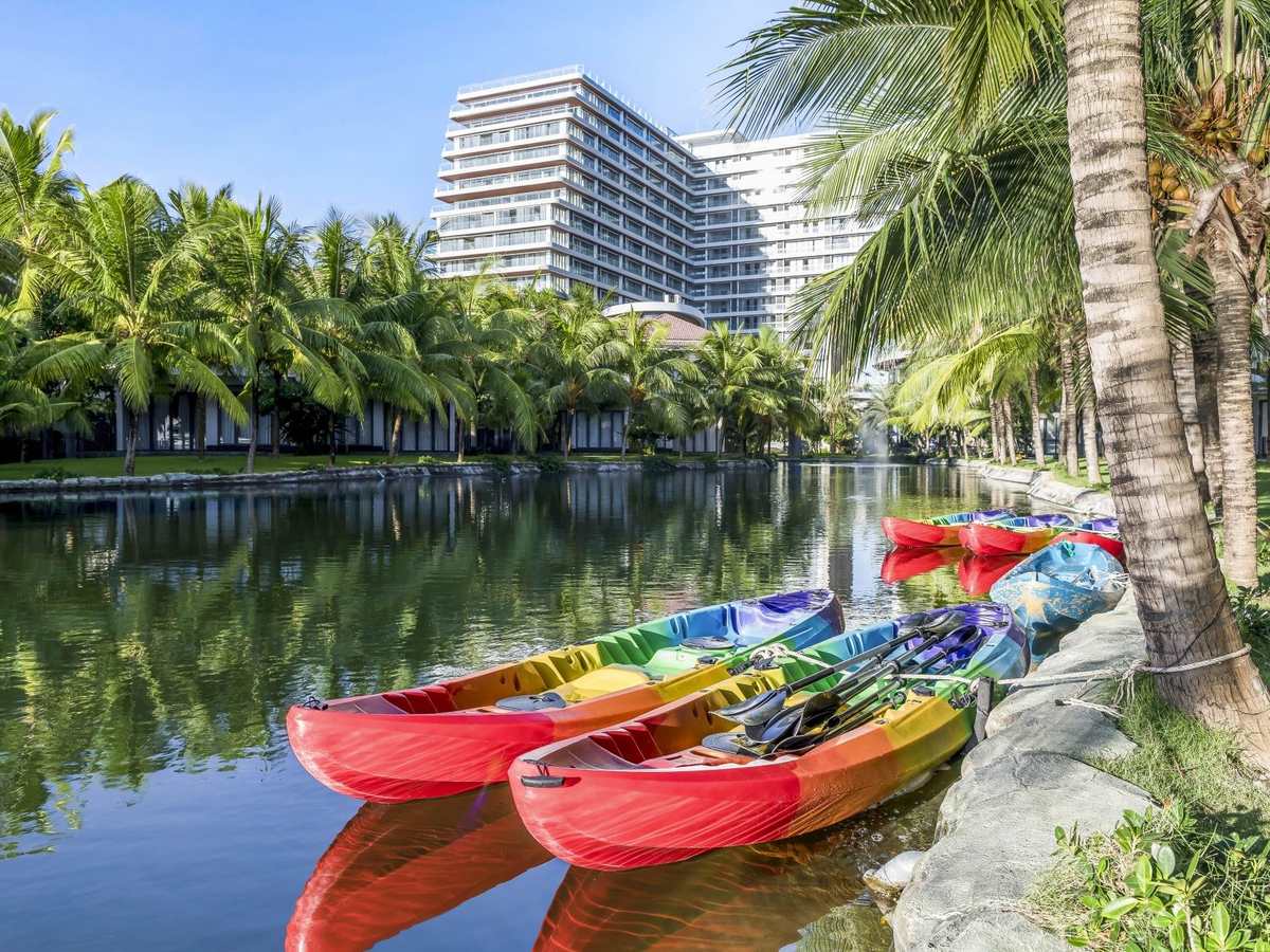 Brightly coloured kayaks moored on a calm palm-lined waterway, with a tall white building behind