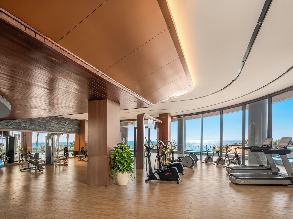 Gym with treadmills, cross-trainers and weight machines on a wooden floor, glass walls facing the sea