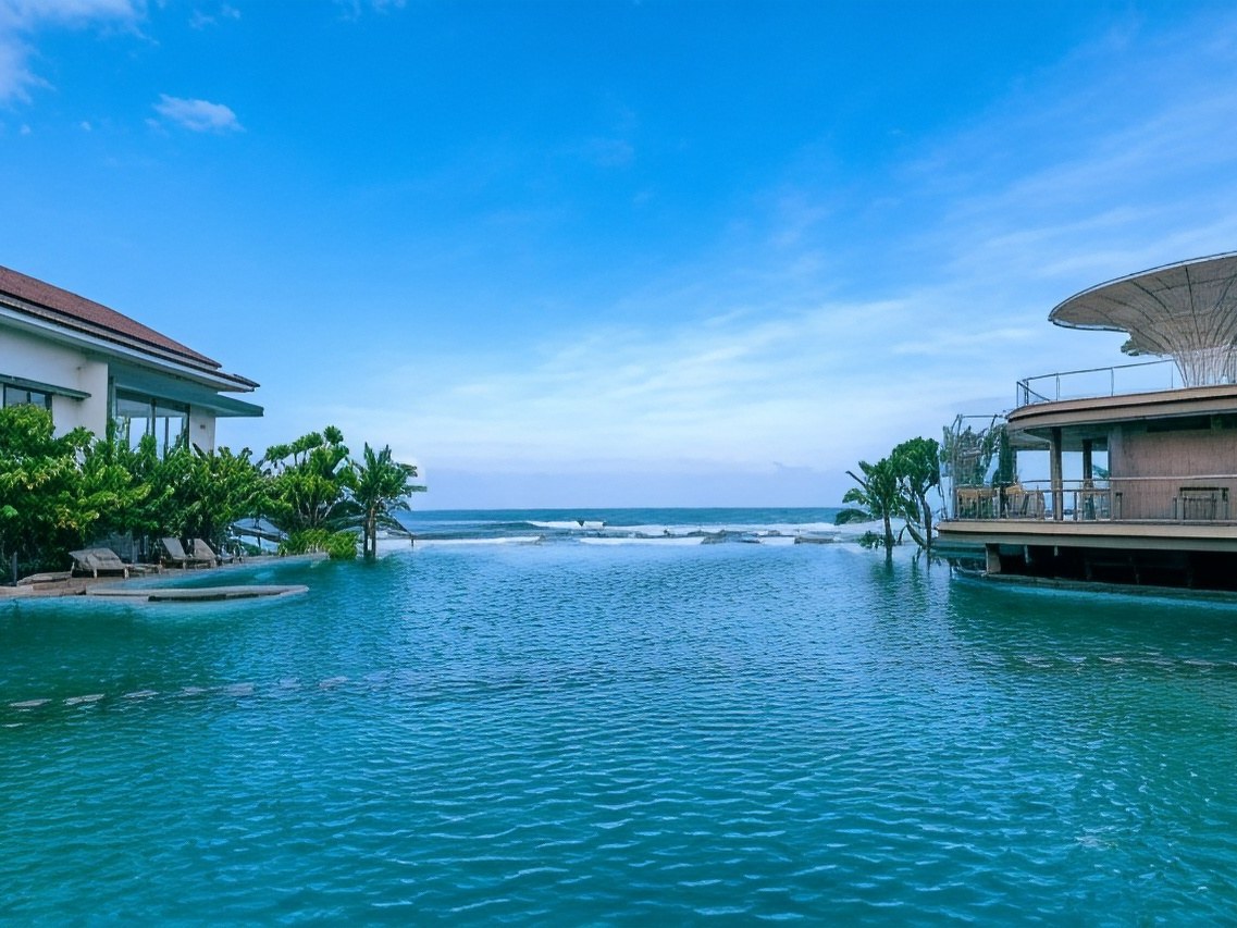 Infinity pool running out towards the sea, with sun loungers on one side and a canopied bar on the other