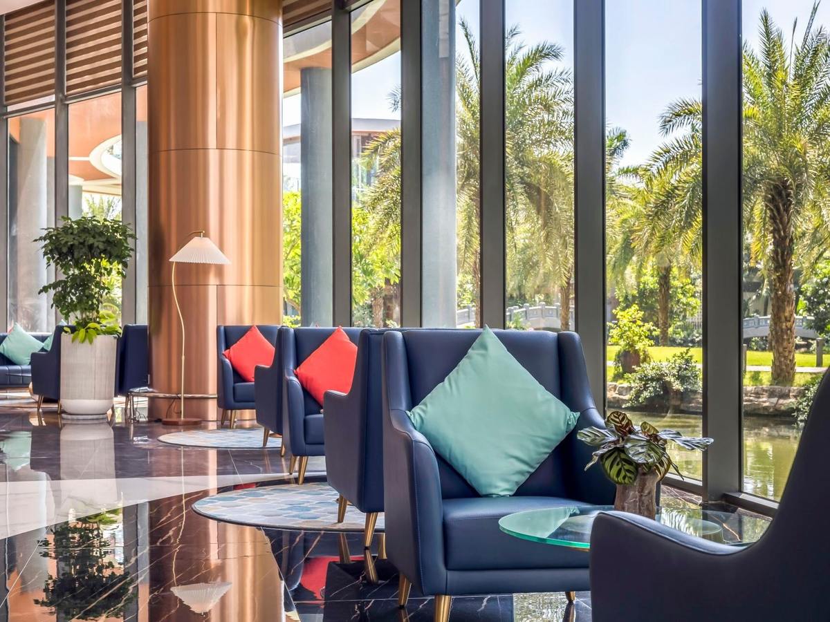 Navy armchairs with coral and turquoise cushions beside floor-to-ceiling windows facing palm trees