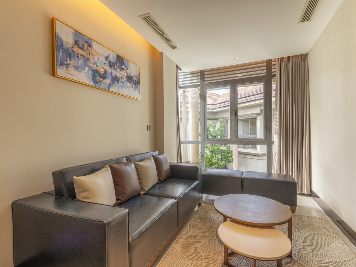 Small living room with a dark leather sofa, two round coffee tables and a window looking onto red-tiled roofs