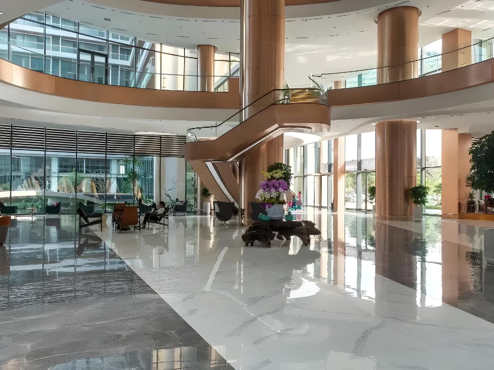 Bright double-height lobby with a marble floor, copper columns and a curved staircase up to a glass-walled gallery