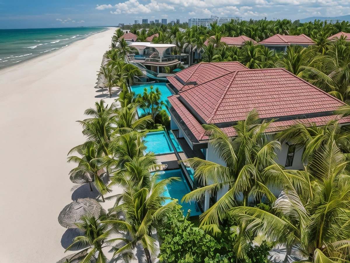 Wide sandy beach beside red-roofed villas with stepped private pools behind a row of palm trees