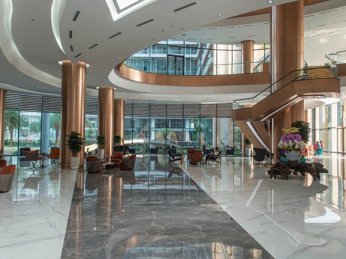 Large lobby with a polished marble floor, copper columns, a curved staircase and armchairs by tall windows