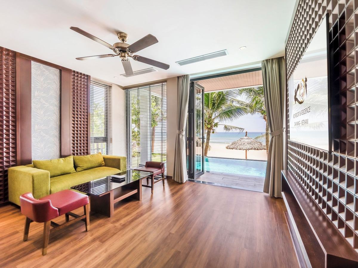 Villa living room with a green sofa, ceiling fan and open glass doors leading to a private pool and the beach