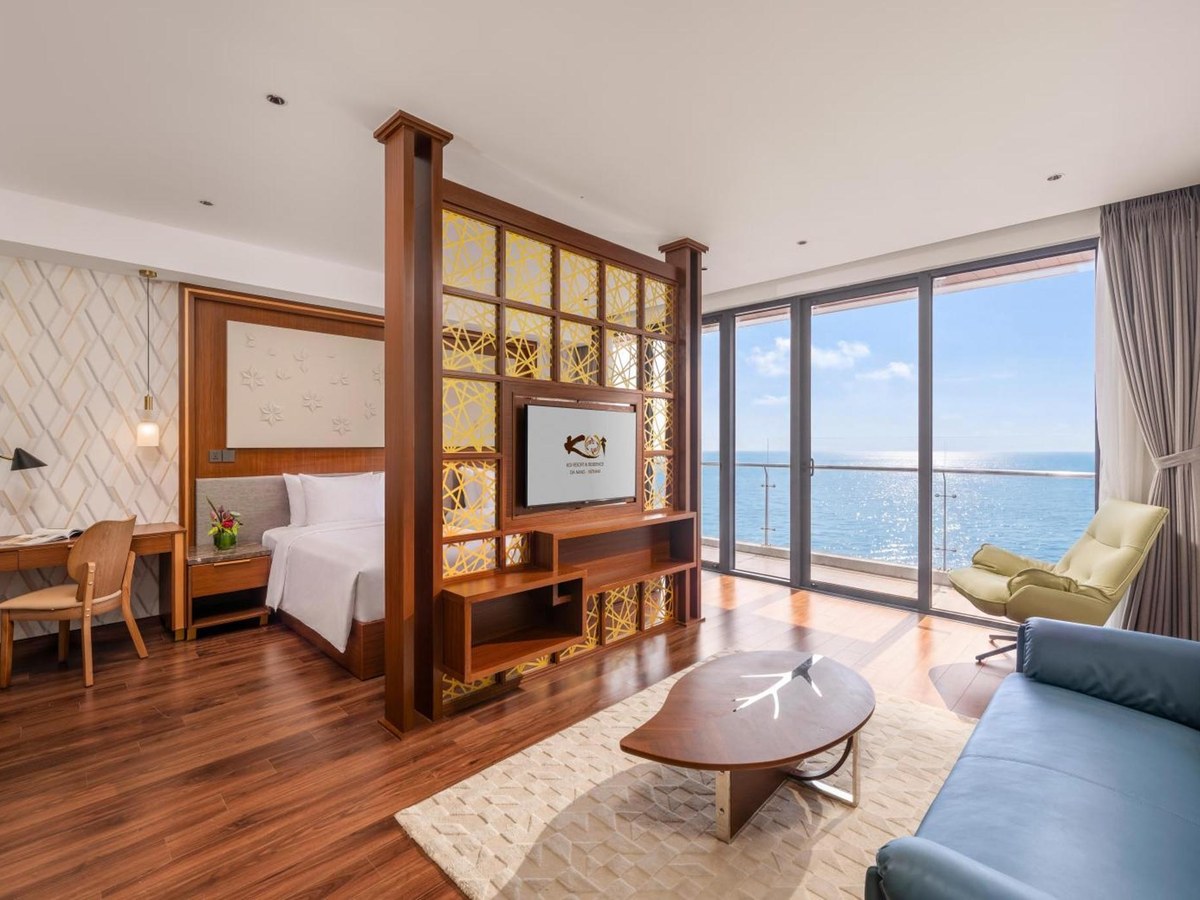 Suite có hai giường đơn sau vách gỗ, sofa xanh dương và cửa sổ rộng nhìn ra biển