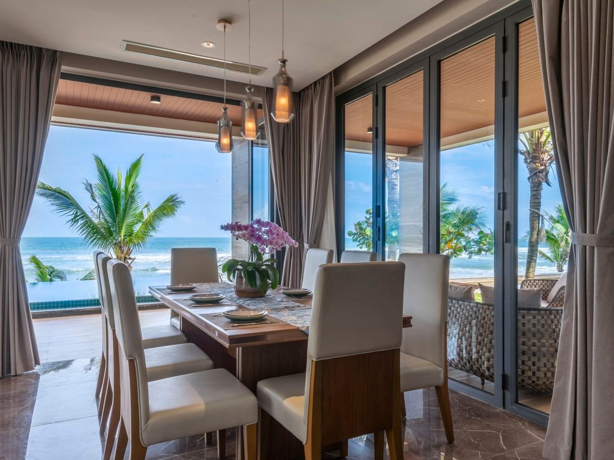 Bàn ăn trong villa cạnh cửa kính mở, bên ngoài là hàng cọ và biển